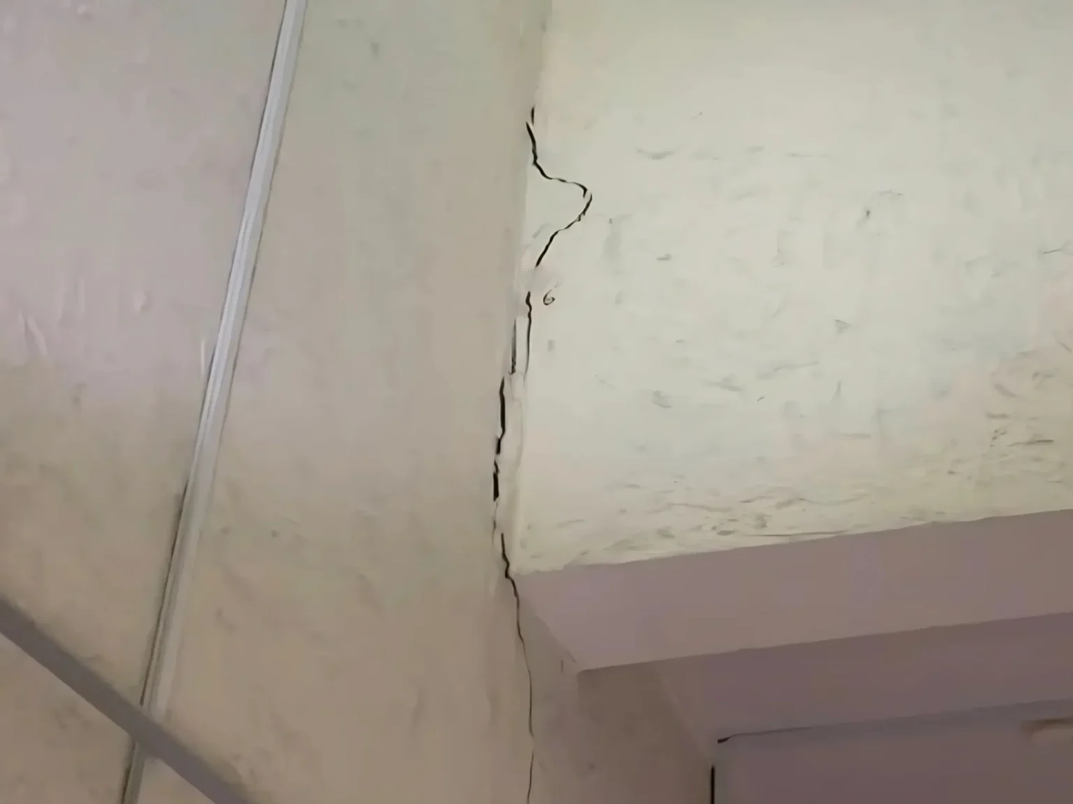 Vertical wall crack at ceiling corner indicating foundation subsidence and structural damage.